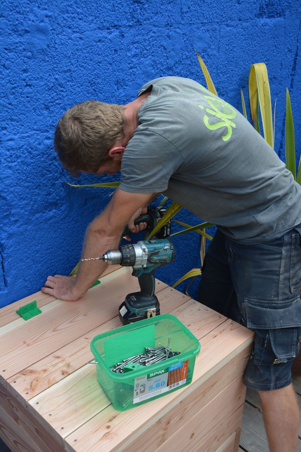 Jardinier SICLE assemblant un bac en bois devant un mur bleu